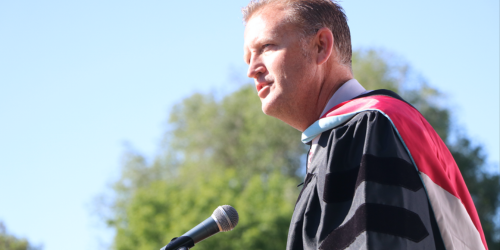 Man in graduation robes speaking at a podium